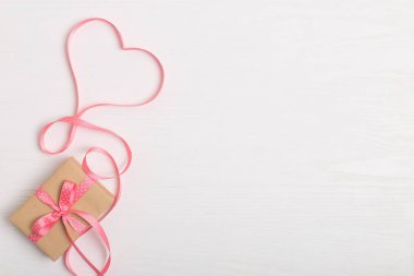 Kraft kağıt ve pembe bir kurdele Beyaz ahşap bir masa üzerinde bir hediye. Metin, kopya alanı, Sevgililer günü kartpostal için yer.