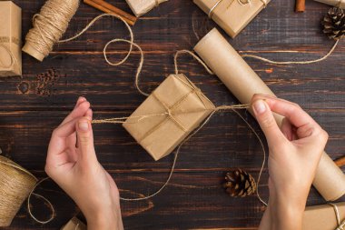 Women's hands making a gift of craft paper. Against the background of dried orange, cinnamon, pine cones, anise on a wooden table.