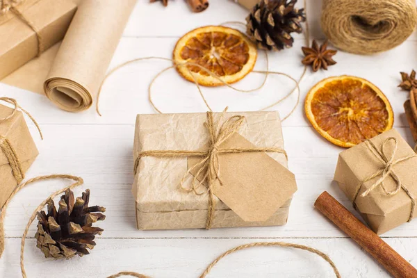 Gifts from craft paper, dried orange, cinnamon, pine cones, anise on a white table. The original decor for Christmas.