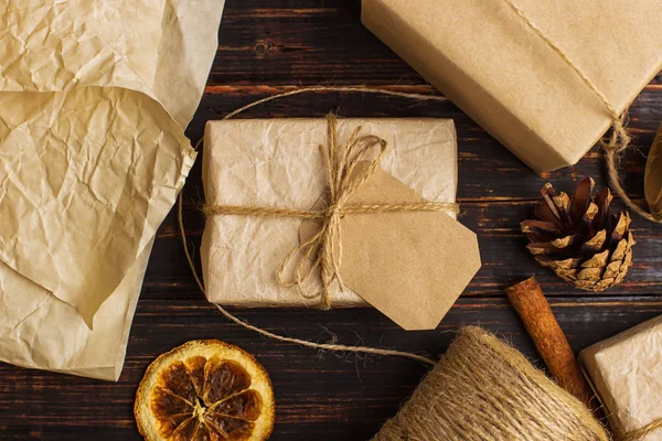 Gift of craft paper against the background of dried orange, cinnamon, pine cones, anise on a wooden table.