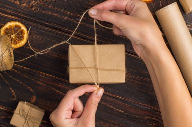 Women's hands making a gift of craft paper. Against the background of dried orange, cinnamon, pine cones, anise on a wooden table.