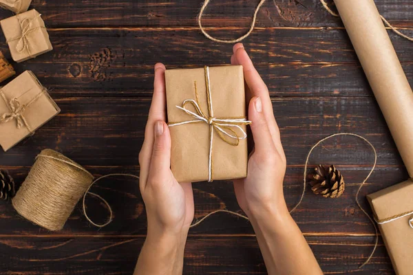 Women\'s hands hold a gift of craft paper. Against the background of dried orange, cinnamon, pine cones, anise on a wooden table.