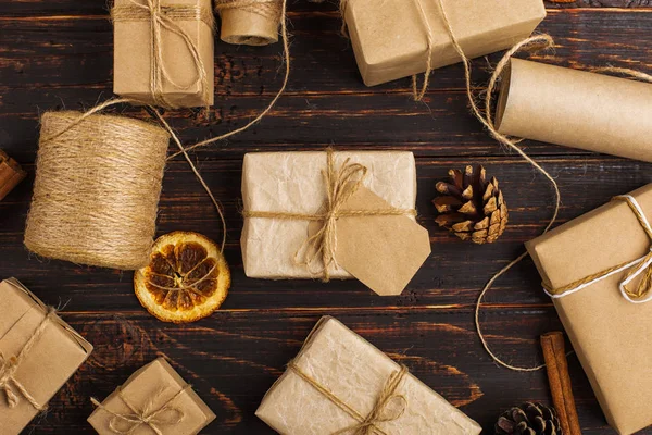 Gift of craft paper against the background of dried orange, cinnamon, pine cones, anise on a wooden table.