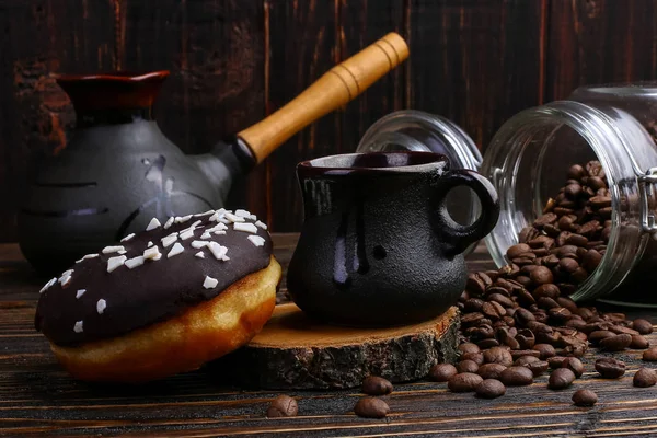 Donut with black icing and chocolate powder and an authentic cup of strong coffee. A can coffee beans and poured grains.