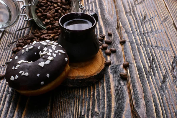 Donut with black icing and chocolate powder and an authentic cup of strong coffee. A can coffee beans and poured grains.