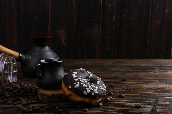 Donut with black icing and chocolate powder and an authentic cup of strong coffee. A can coffee beans and poured grains.