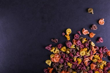 Doğal bitkisel boya ilavesi ile çok renkli makarna. Siyah beton masaya dağınık. Üstten Görünüm, kopya alanı.
