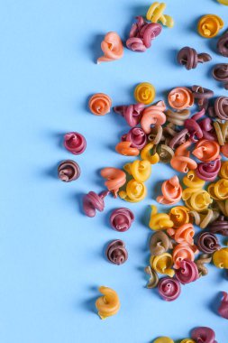 Doğal bitkisel boya ilavesi ile çok renkli makarna. Mavi arka plan üzerinde dağınık. Üstten Görünüm, desen.