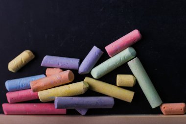 Multicolored crayons lie on black chalk board, copy space. The concept of school, education and childhood. clipart