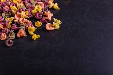 Doğal bitkisel boya ilavesi ile çok renkli makarna. Siyah beton masaya dağınık. Üstten Görünüm, kopya alanı.