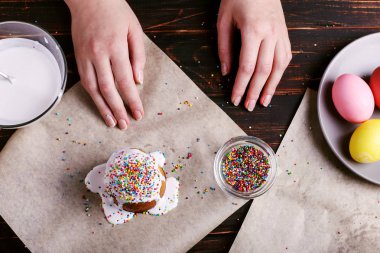 Kız Paskalya pişirme hazırlar, pasta buzlanma ile smear ve renkli toz ile sprinkles. Mutfak masasında karanlık bir arka plan üzerinde tatil için hazırlanıyor.
