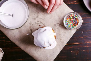 Kız Paskalya pişirme hazırlar, pasta buzlanma ile smear ve renkli toz ile sprinkles. Mutfak masasında karanlık bir arka plan üzerinde tatil için hazırlanıyor.