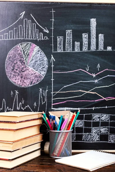 Books on the table against the background of a chalkboard on which are drawn graphs and charts of growth and decline. Business training school.