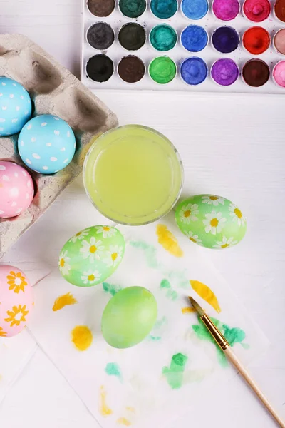Рука розмальовувала великодні яйця, фарби та пензлі на білому столі. Підготовка до свята . — стокове фото