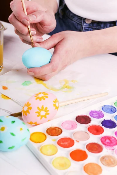 Рука розмальовувала великодні яйця, фарби та пензлі на білому столі. Підготовка до свята. Дівчата руки малюють візерунок . — стокове фото