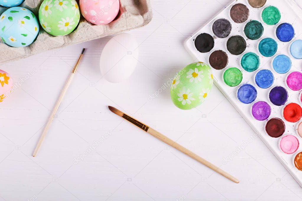 Hand painted Easter eggs, paints and brushes on a white table. Preparation for the holiday.