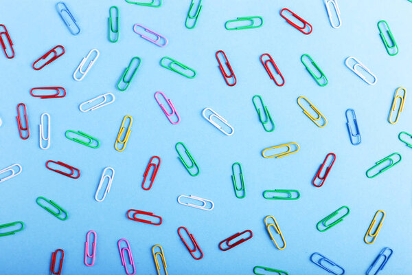 Multicolored paper clips on a blue background, pattern, copy space.