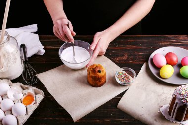Kız Paskalya pişirme hazırlar, pasta buzlanma ile smear ve renkli toz ile sprinkles. Mutfak masasında karanlık bir arka plan üzerinde tatil için hazırlanıyor.