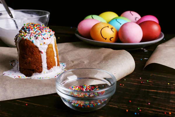 Пасхальна випічка з глазур'ю, кольоровим порошком та яйцями. Готуючись до свята на кухонному столі, на темному тлі . — стокове фото