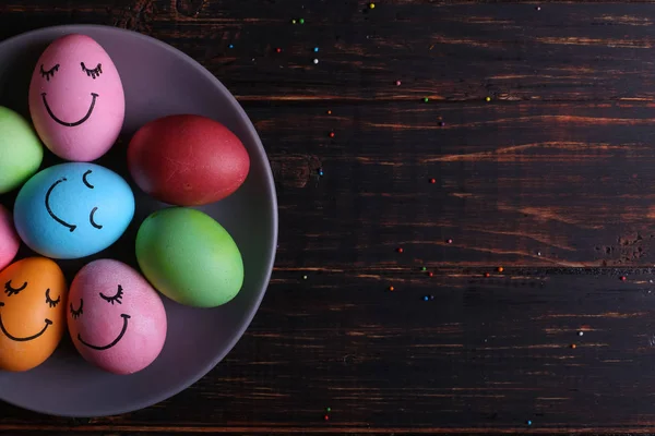 Easter eggs with cute faces on the plate. Preparing for the holiday on the kitchen table, on a dark background, copy space.