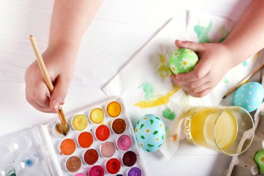 Çocuk el boyalı Paskalya yumurtaları, boyar ve beyaz bir masada fırçalar. Tatil için hazırlık. Kızlar el bir desen çizmek.