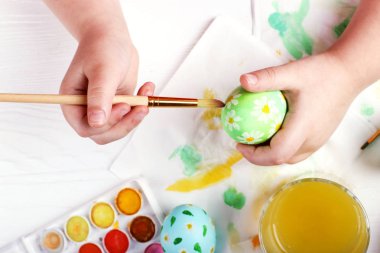 Çocuk el boyalı Paskalya yumurtaları, boyar ve beyaz bir masada fırçalar. Tatil için hazırlık. Kızlar el bir desen çizmek.