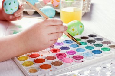 Çocuk el boyalı Paskalya yumurtaları, boyar ve beyaz bir masada fırçalar. Tatil için hazırlık. Kızlar el bir desen çizmek.