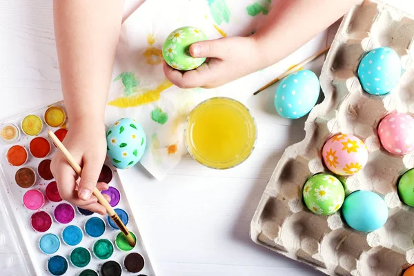 Ребенок вручную рисовал пасхальные яйца, краски и кисти на белом столе. Подготовка к празднику. Девушки руки рисуют шаблон . — стоковое фото