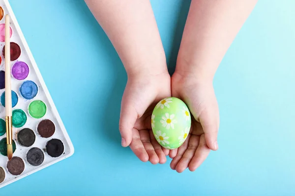 Дитячі руки тримають прикрашене пасхальне яйце на синьому фоні . — стокове фото