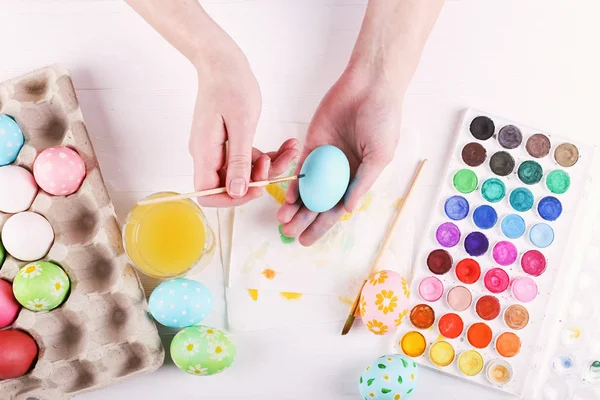 Рука розмальовувала великодні яйця, фарби та пензлі на білому столі. Підготовка до свята. Дівчата руки малюють візерунок . — стокове фото