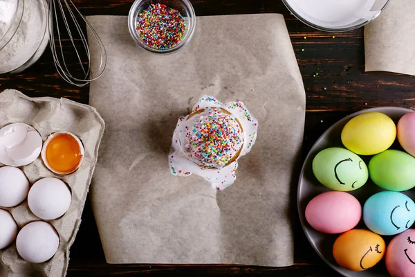 Пасхальная выпечка с глазурью и цветной порошок и яйца. Подготовка к празднику на кухонном столе, на темном фоне . — стоковое фото