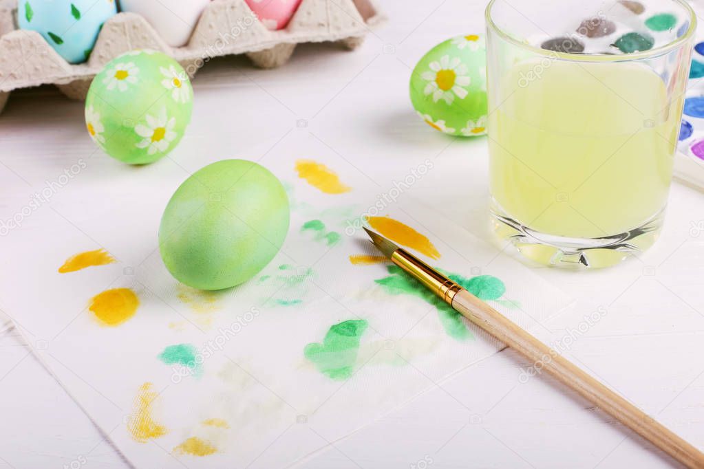 Hand painted Easter eggs, paints and brushes on a white table. Preparation for the holiday.
