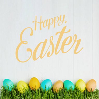 Beyaz bir tabloda, üstten görünüm çimenlerin üzerinde renkli Paskalya yortusu yumurta