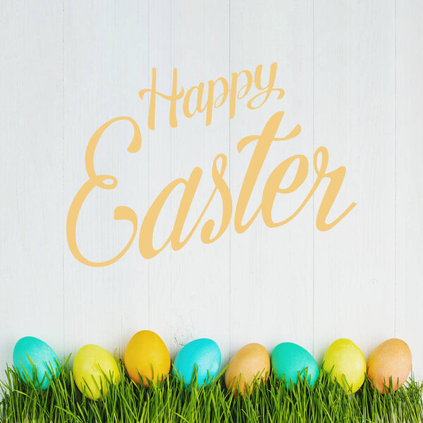 colored Easter eggs on the grass, on a white table, top view