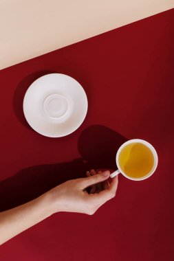 Seramik bardak çay, kırmızı arka plan ile. Güneş, sabah sanat kavramı ve enerji şarj sert gölgesinde. Kız el için kupa ulaşır.