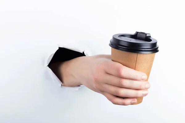 Vrouwelijke hand uit het gat in de paperman, houdt een bruinglas koffie met hem. Isoleren op witte achtergrond. — Stockfoto