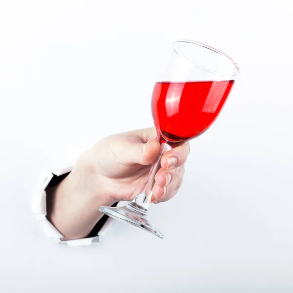 Mano femenina fuera del agujero en el papelero, sosteniendo una copa de vino tinto. Aislar sobre fondo blanco . —  Fotos de Stock