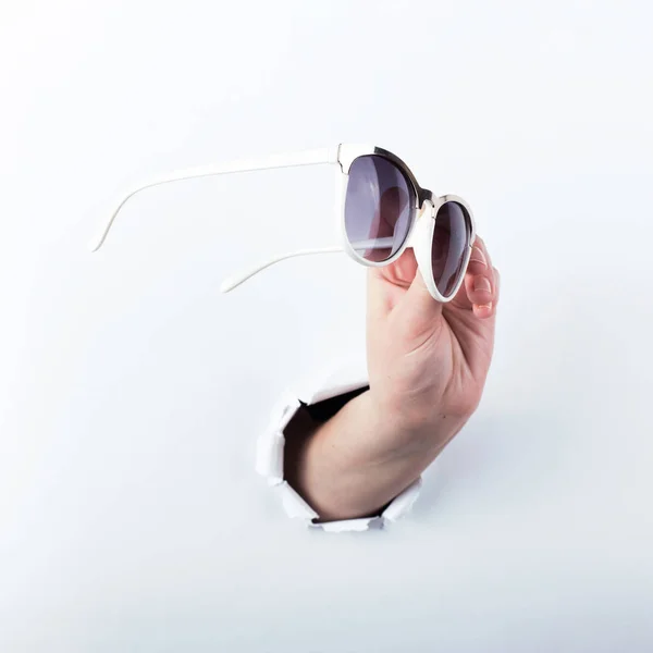 Mano femminile fuori dal buco nel fermacarte, tenendo gli occhiali da sole per la vista. Isolato su sfondo bianco . — Foto Stock