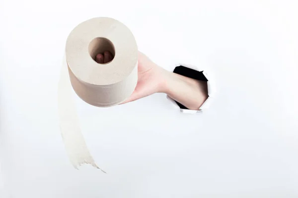 Mano femenina fuera del agujero en el papelero, sosteniendo un rollo de papel higiénico. Aislar sobre fondo blanco . — Foto de Stock