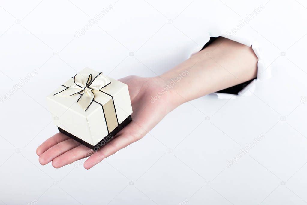 Female hand out of a hole in paper, holds a small gift. Isolate on white background.