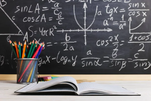 Schulbank im Klassenzimmer, mit Büchern auf dem Hintergrund einer Kreidetafel mit geschriebenen Formeln. Soncept Lehrertag. — Stockfoto