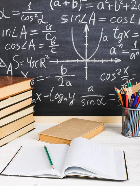 Школьный стол в классе, с книгами на фоне меловой доски с письменными формулами. День учителя Сонсепта . — стоковое фото