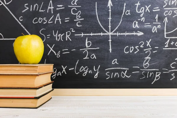 School desk in classroom, with books on background of chalk board with written formulas. Soncept Teacher\'s Day.