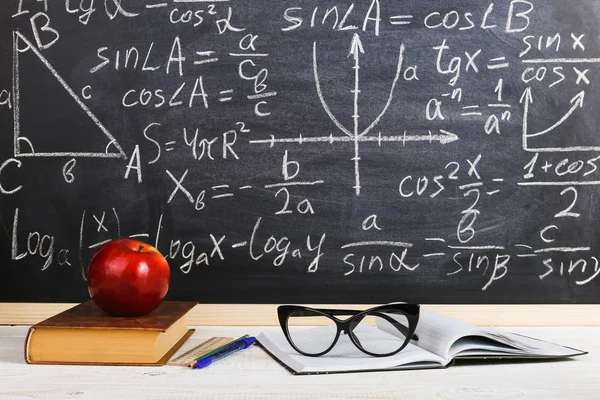 School desk in classroom, with books on background of chalk board with written formulas. Soncept Teacher\'s Day.