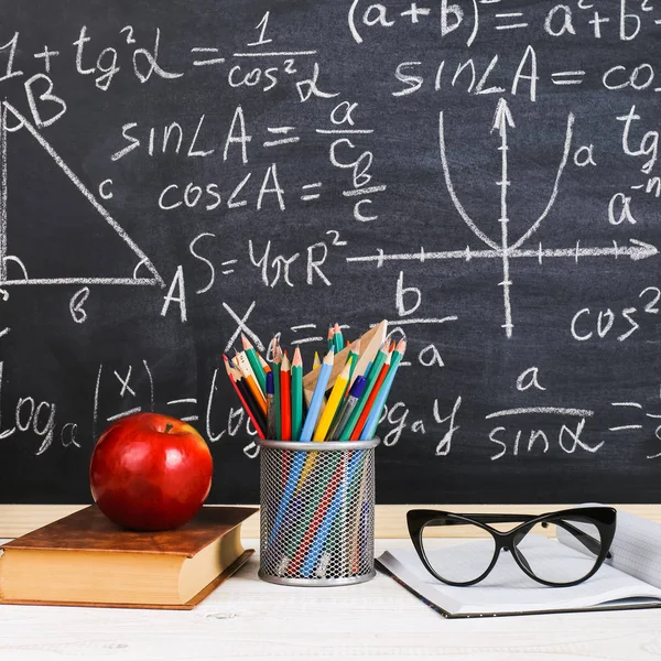 Schulbank im Klassenzimmer, mit Büchern auf dem Hintergrund einer Kreidetafel mit geschriebenen Formeln. Soncept Lehrertag. — Stockfoto