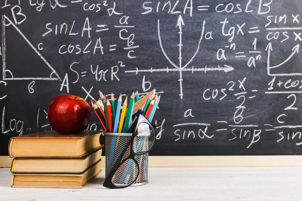 Schulbank im Klassenzimmer, mit Büchern auf dem Hintergrund einer Kreidetafel mit geschriebenen Formeln. Soncept Lehrertag. — Stockfoto