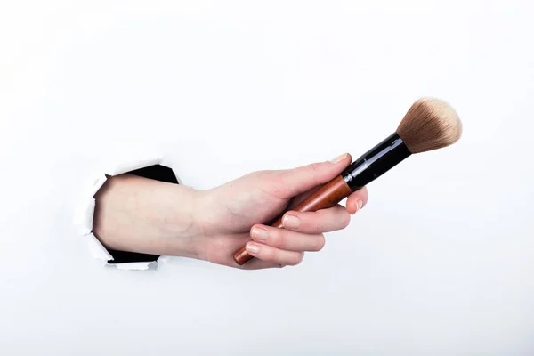 Mano femenina fuera de un agujero en papel, sosteniendo un cepillo de polvo grande. Aislar sobre fondo blanco . — Foto de Stock