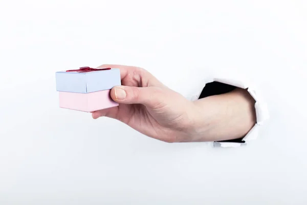 Weibliche Hand aus einem Loch in Papier, hält ein kleines Geschenk. isolieren auf weißem Hintergrund. — Stockfoto