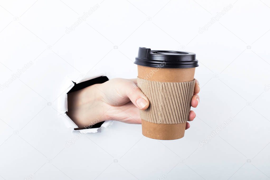Female hand out of the hole in the paperman, keeps a brown glass of coffee with him. Isolate on white background.