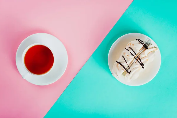 Торт с безе на блюдце и чашка чая на бумажном фоне пастельного цвета . — стоковое фото
